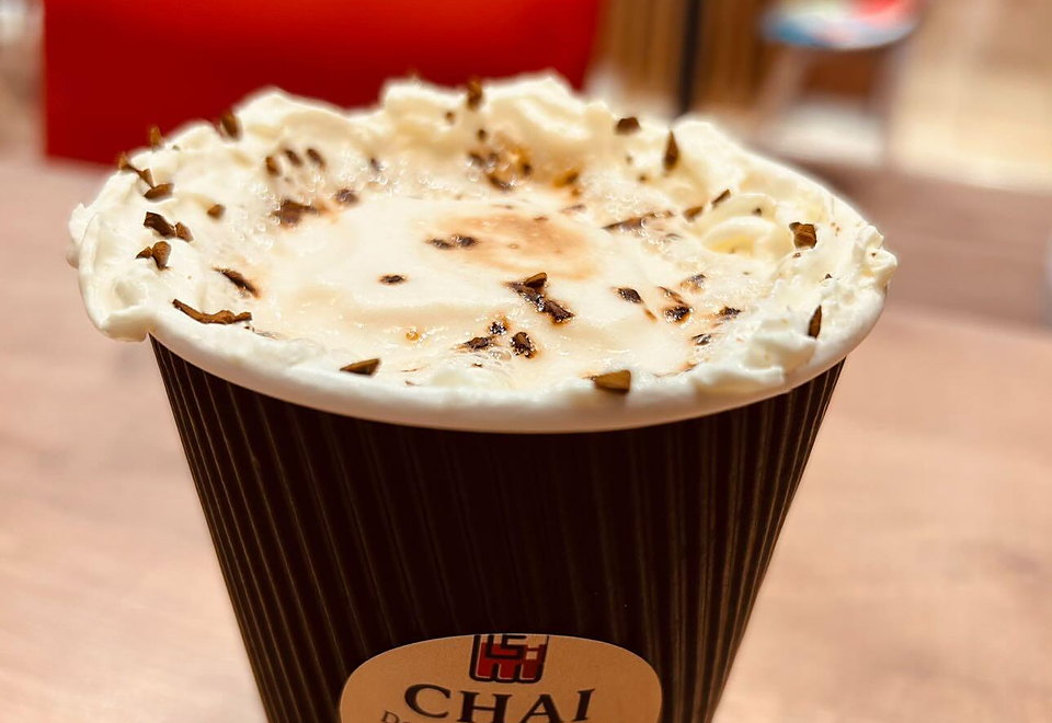 Latte im CHAI Becher mit Sahnehaube und Pistazien