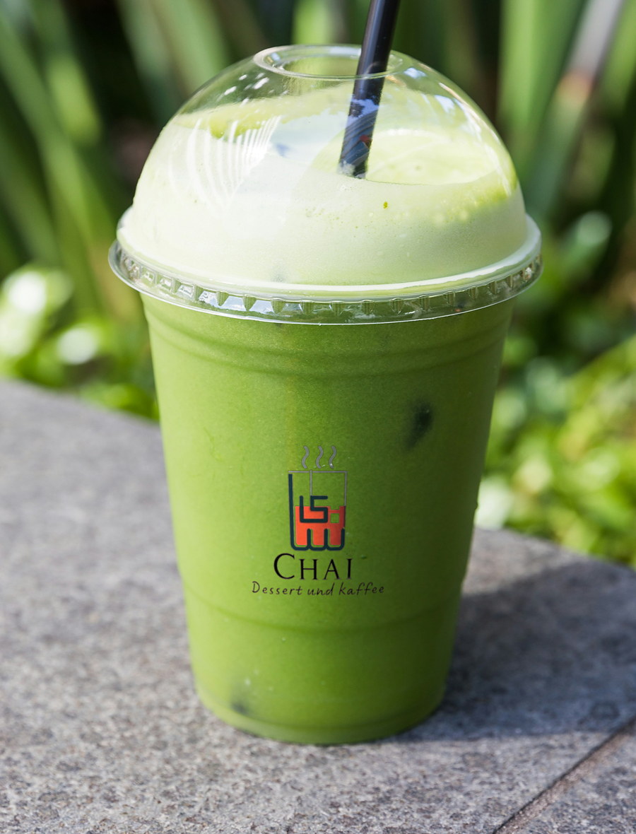 Eis Matcha Latte im CHAI Becher mit Kuppeldeckel, draußen auf einer Steinmauer